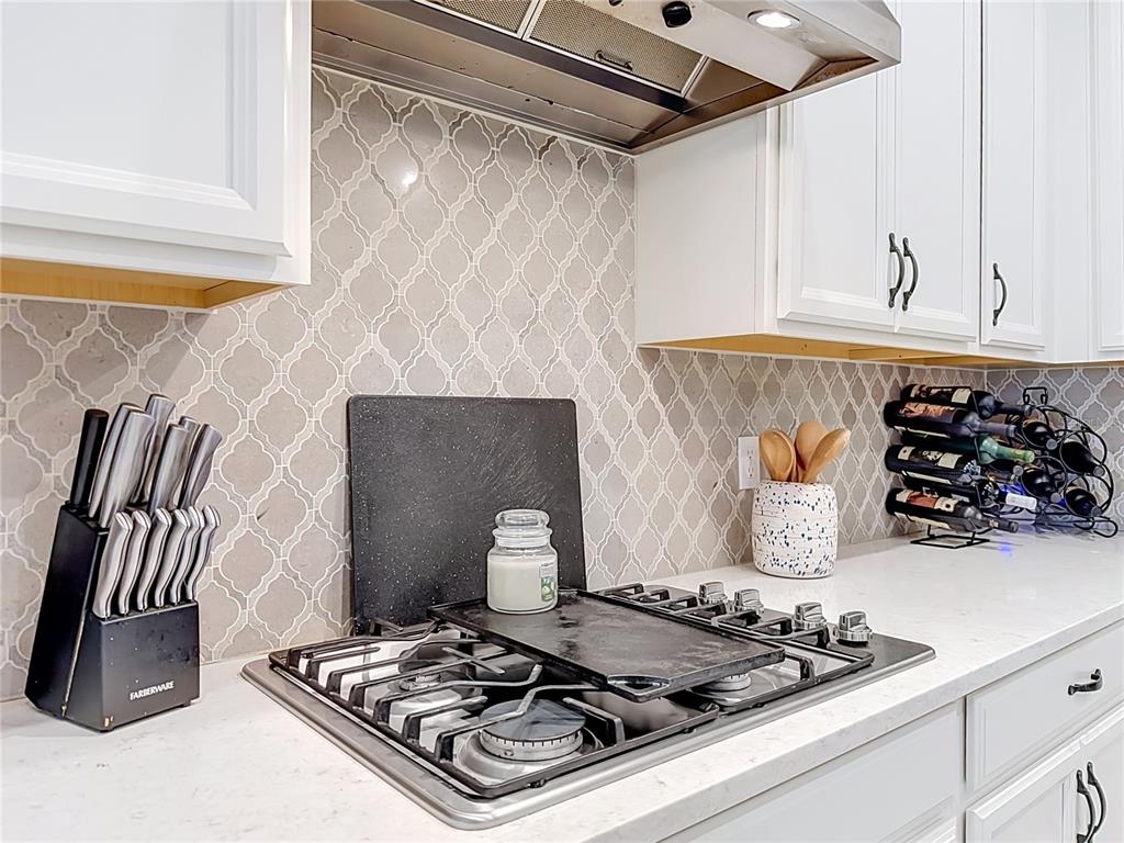 A kitchen features white cabinets, a patterned tile backsplash, and a stainless steel gas cooktop — 2599 RIDGETOP LN, CLERMONT, FL