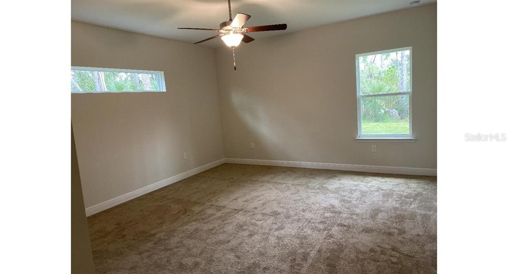 An empty bedroom features beige carpet, light-colored walls, a ceiling fan, and two windows — 5519 BAKER ROAD, NORTH PORT, FL