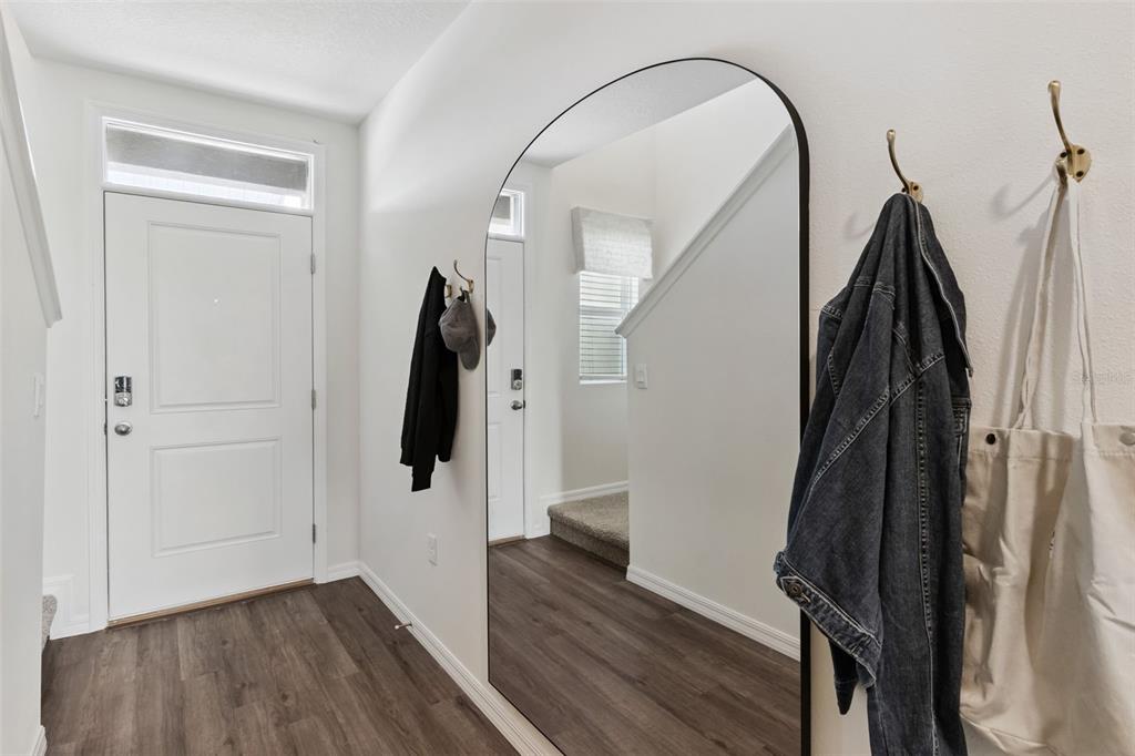 A bright entryway features a white door, wood-look flooring, a large arched mirror, and hooks — 4266 BUTTERSCOTCH CIRCLE, LAKELAND, FL