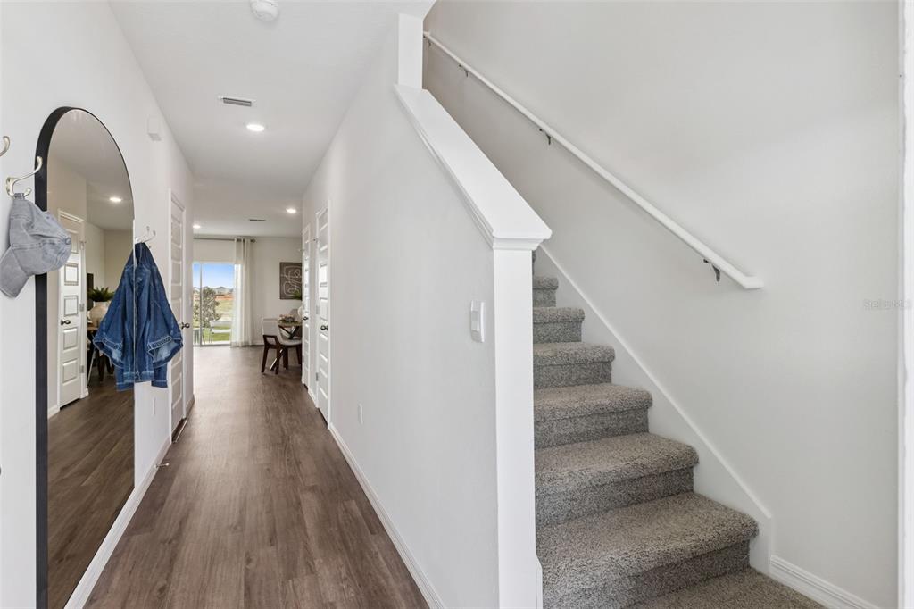 A hallway with wood-look flooring leads to a dining area past a carpeted staircase — 4266 BUTTERSCOTCH CIRCLE, LAKELAND, FL