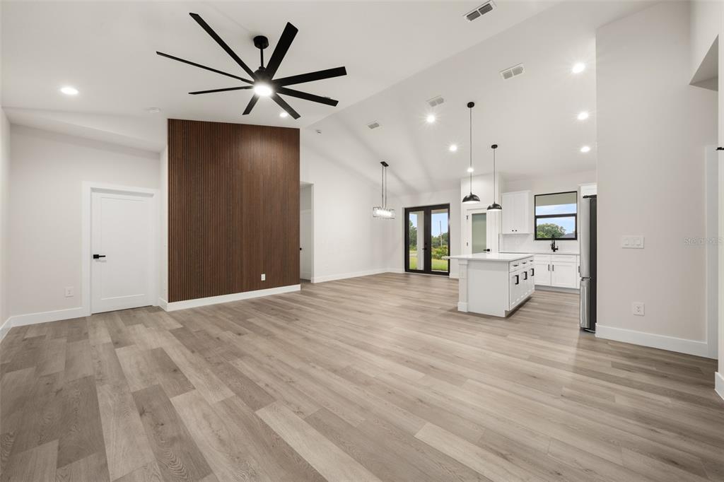 An open-concept living area features a wood-slat accent wall, vaulted ceilings, and a modern kitchen — 5846 SAN JUAN DRIVE, SEBRING, FL