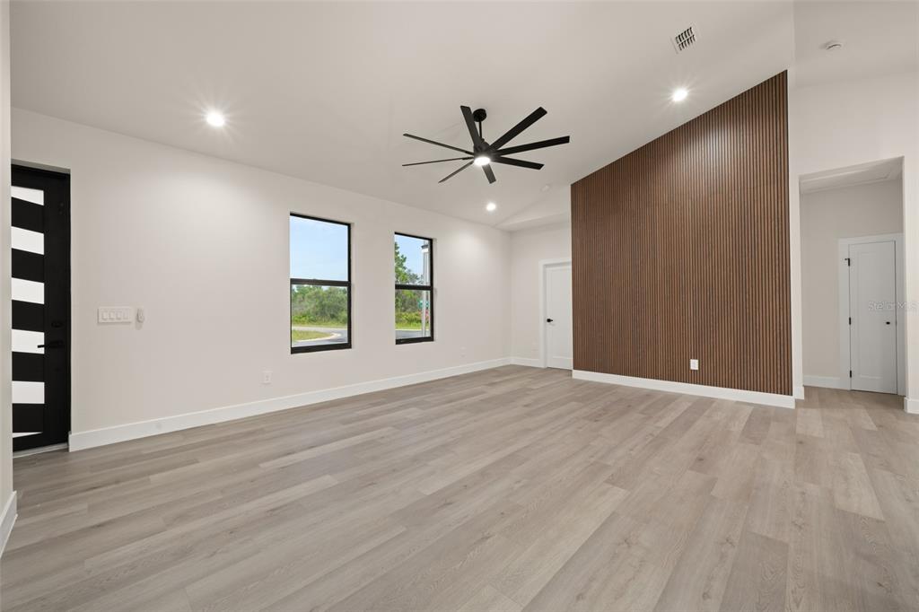 A modern living room features light wood-look flooring, a slatted wood accent wall, and a ceiling fan — 5846 SAN JUAN DRIVE, SEBRING, FL
