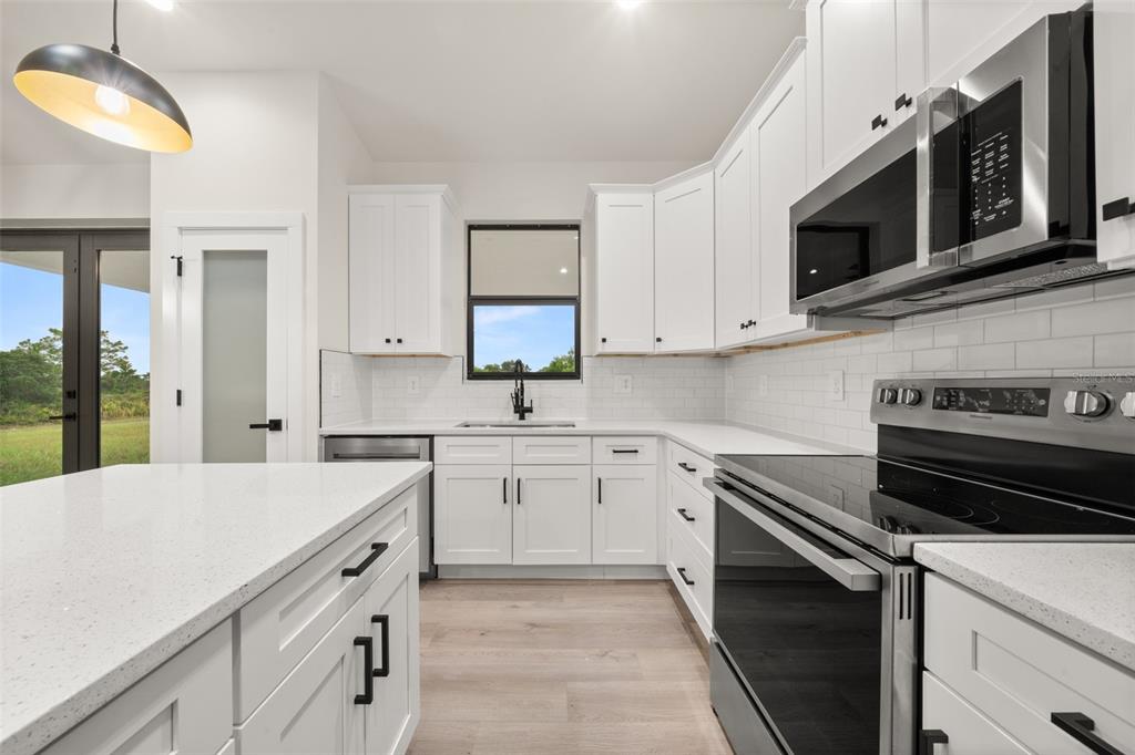A modern kitchen features white cabinets, quartz countertops, stainless steel appliances, and light wood flooring — 5846 SAN JUAN DRIVE, SEBRING, FL