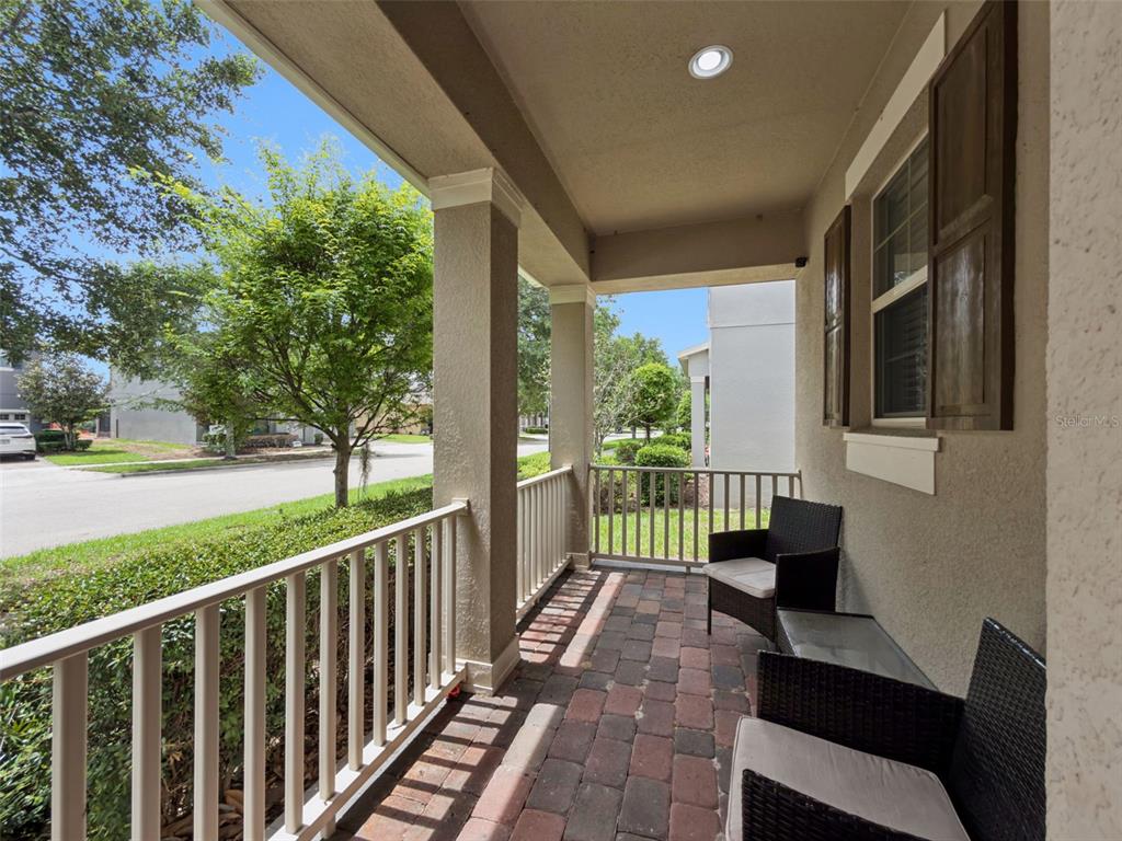 A covered front porch features brick pavers, white railings, and two wicker chairs — 16197 WIND VIEW LANE, WINTER GARDEN, FL