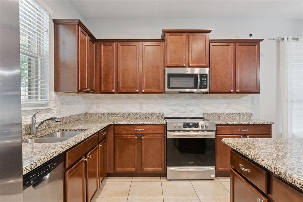 A kitchen with wood cabinets, granite countertops, stainless steel appliances, and a white textured backsplash — 16197 WIND VIEW LANE, WINTER GARDEN, FL