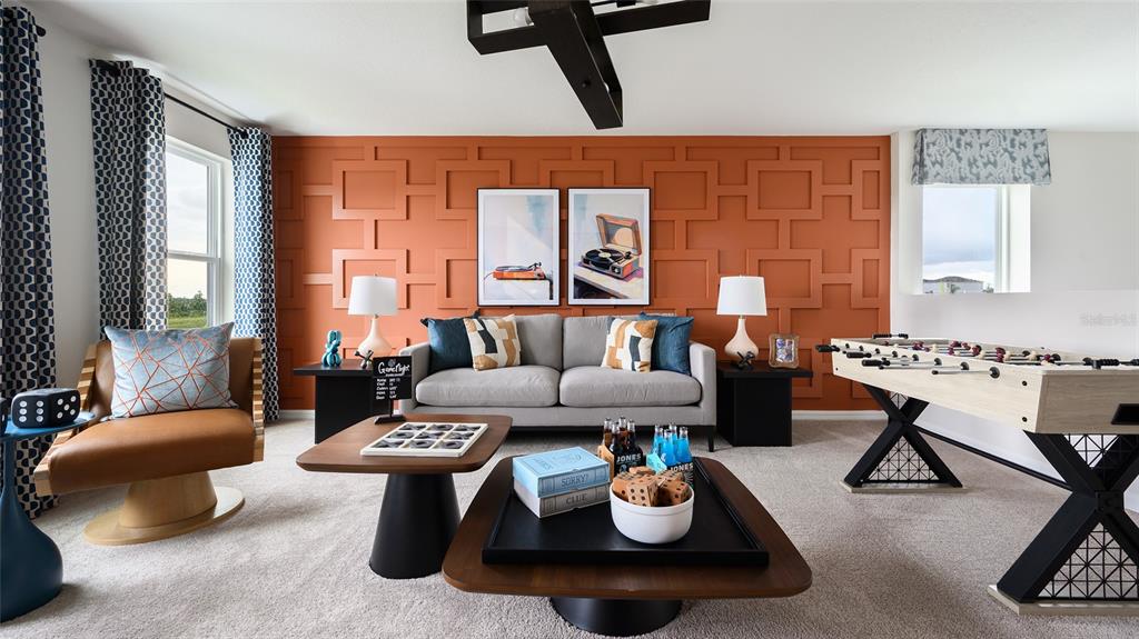 A game room features a gray sofa, a foosball table, and a geometric orange accent wall — 36676 THORNHEDGE DRIVE, ZEPHYRHILLS, FL