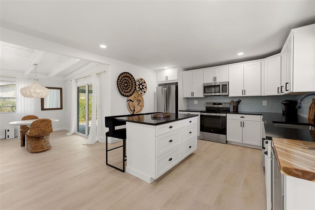 A kitchen features white cabinets, a black island, stainless steel appliances, and light wood flooring — 1757 MOVA STREET, SARASOTA, FL