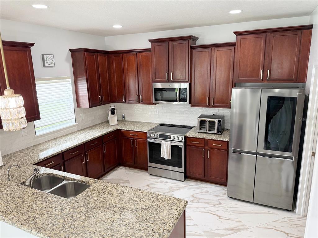 A kitchen features dark wood cabinets, granite countertops, stainless steel appliances, and light tile flooring — 12236 FAIRLAWN DRIVE, RIVERVIEW, FL