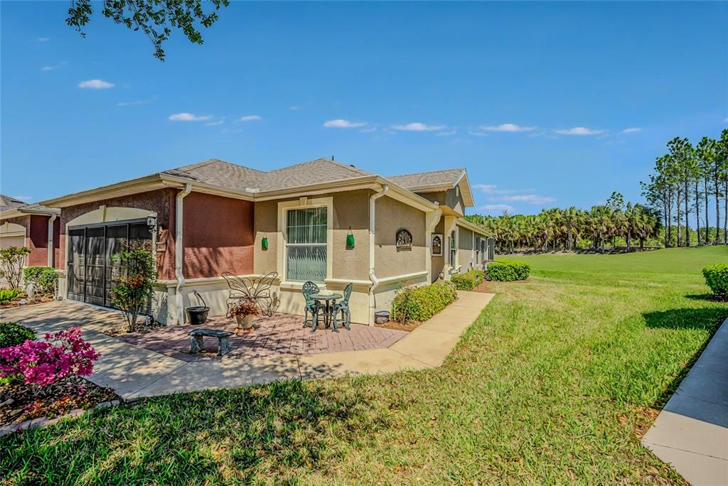 A tan house with a brick patio, a garage, and a large grassy backyard — 9077 SW 70TH LOOP, OCALA, FL