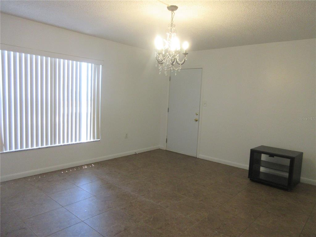 A dining room features tile flooring, a crystal chandelier, and a large window with blinds — 2410 SE 16TH AVENUE UNIT H, OCALA, FL