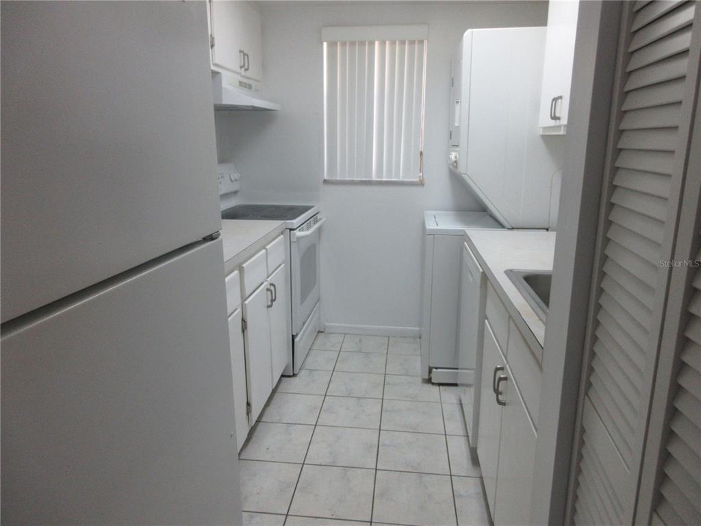 A narrow galley kitchen features white cabinets, white appliances, and light-colored tile flooring — 2410 SE 16TH AVENUE UNIT H, OCALA, FL