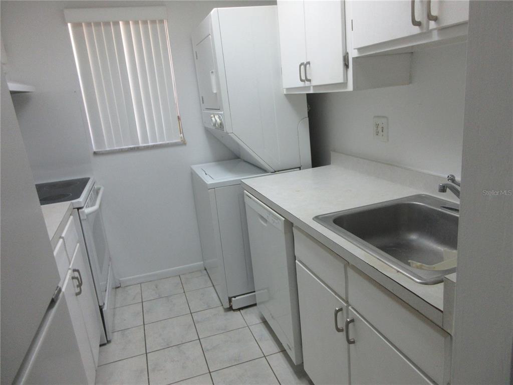 A small kitchen features white cabinets, a stacked washer-dryer unit, and white tile flooring — 2410 SE 16TH AVENUE UNIT H, OCALA, FL