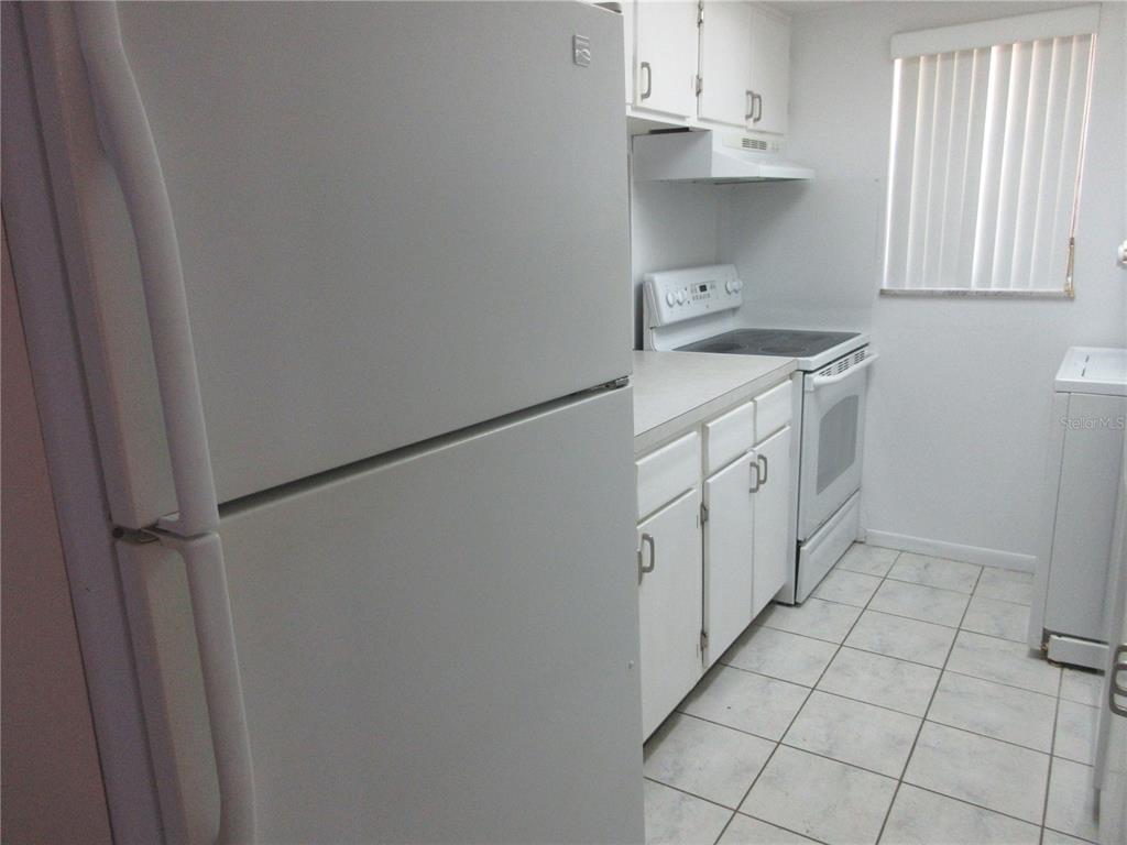 A white kitchen features a refrigerator, stove, cabinets, and tiled flooring — 2410 SE 16TH AVENUE UNIT H, OCALA, FL
