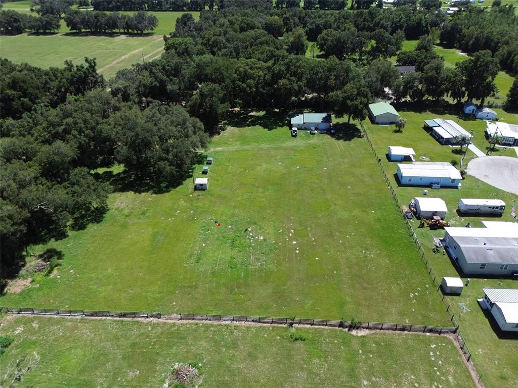 An aerial view shows a large, grassy vacant lot bordered by trees and neighboring residential properties — 10200 CR 749, WEBSTER, FL