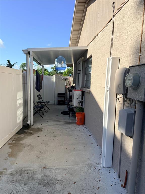 A covered concrete patio area sits beside a house with an exterior electrical meter — 8209 VASSAR CIRCLE, TAMPA, FL