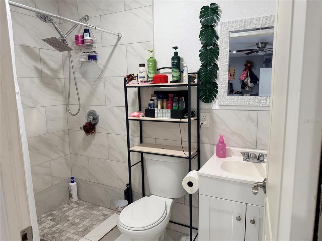 A bathroom features a walk-in shower with white marble-look tiles, a toilet, and a vanity — 8209 VASSAR CIRCLE, TAMPA, FL