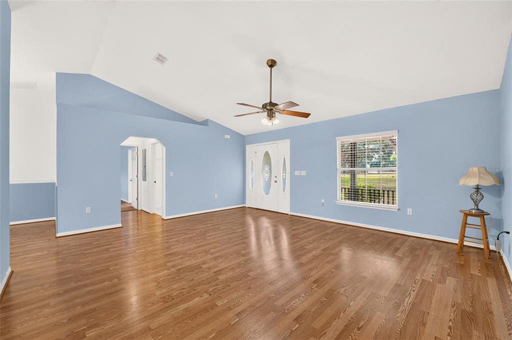 A living room with light blue walls, hardwood floors, a vaulted ceiling, and a ceiling fan — 12499 E HIGHWAY 25, OCKLAWAHA, FL