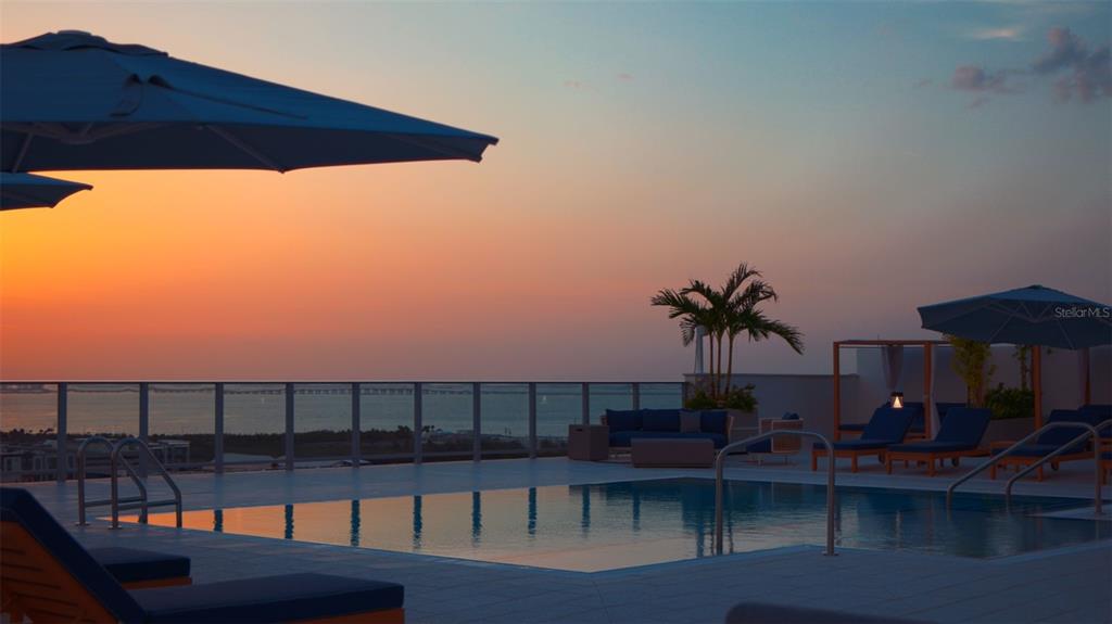A rooftop swimming pool with lounge chairs and umbrellas overlooks the ocean at sunset — 5713 BOWEN DANIEL DRIVE UNIT 606, TAMPA, FL