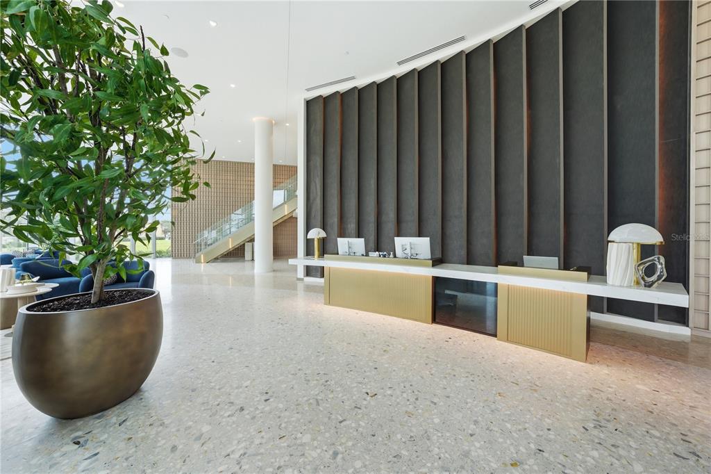 A modern lobby features a long gold reception desk, a large potted plant, and terrazzo flooring — 5713 BOWEN DANIEL DRIVE UNIT 606, TAMPA, FL