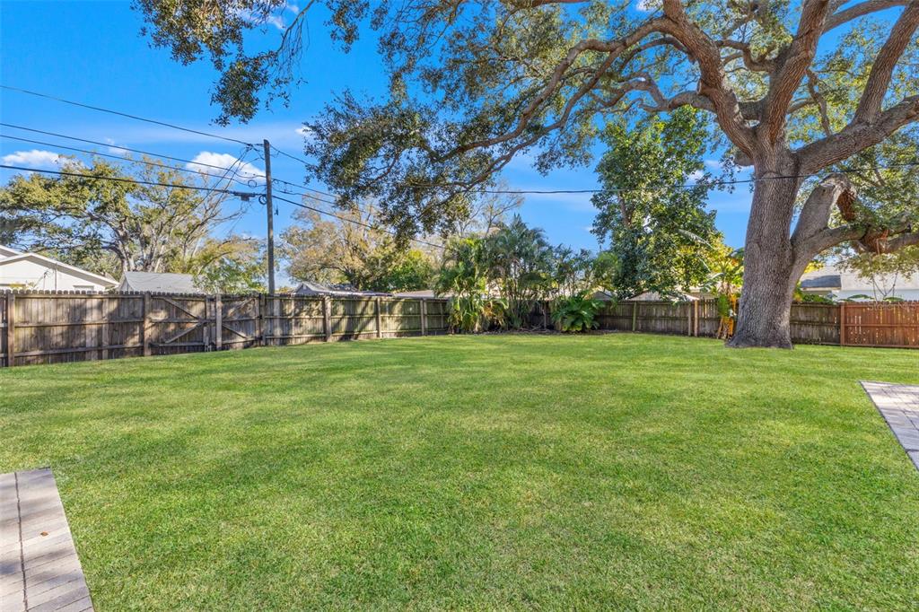 A large, grassy backyard features a wooden privacy fence and a mature oak tree — 1747 26TH AVENUE N, ST PETERSBURG, FL