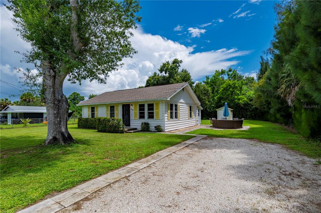 A white house with yellow shutters sits on a grassy lot with a gravel driveway — 809 BURLAND STREET, PUNTA GORDA, FL