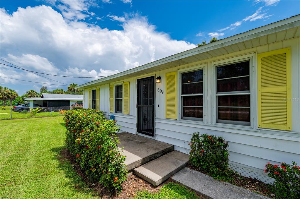A white single-story house features yellow shutters, a concrete porch, and a front door — 809 BURLAND STREET, PUNTA GORDA, FL
