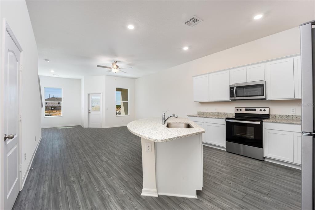 A kitchen with white cabinets, granite countertops, and an island overlooking a gray-floored living area — 697 POPPY LANE, DUNDEE, FL
