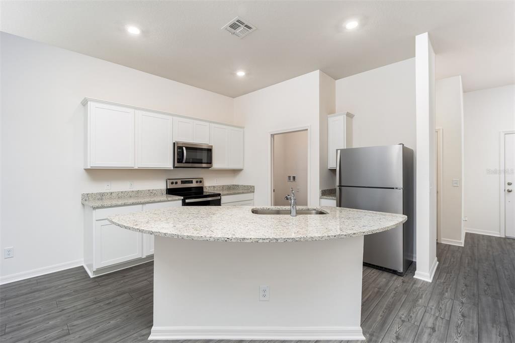 A kitchen features white cabinets, granite countertops, a central island with a sink, and appliances — 697 POPPY LANE, DUNDEE, FL