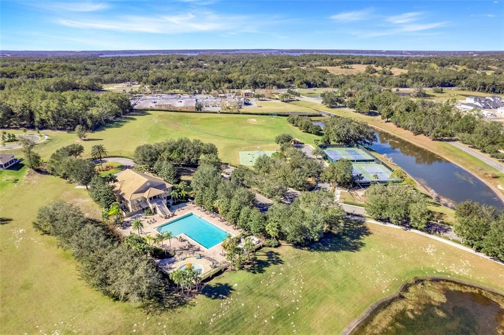 An aerial view shows a house with a pool, tennis courts, and surrounding green space — 5215 TANZANITE DRIVE, MOUNT DORA, FL