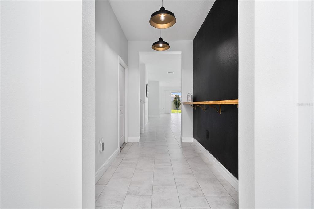 A hallway with light tile flooring, two pendant lights, and a black accent wall — 2591 SEAGIRT WAY, CLERMONT, FL