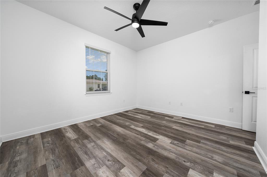 An empty bedroom features white walls, wood-look flooring, a ceiling fan, and a single window — 2591 SEAGIRT WAY, CLERMONT, FL