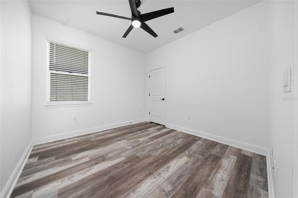 An empty room features white walls, wood-look flooring, a ceiling fan, and a window — 2591 SEAGIRT WAY, CLERMONT, FL