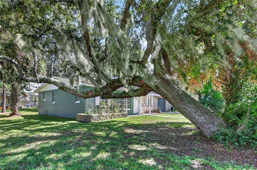 A green house exterior features a screened-in porch and a landscaped rock garden area — 2071 CANAL ROAD, DELTONA, FL