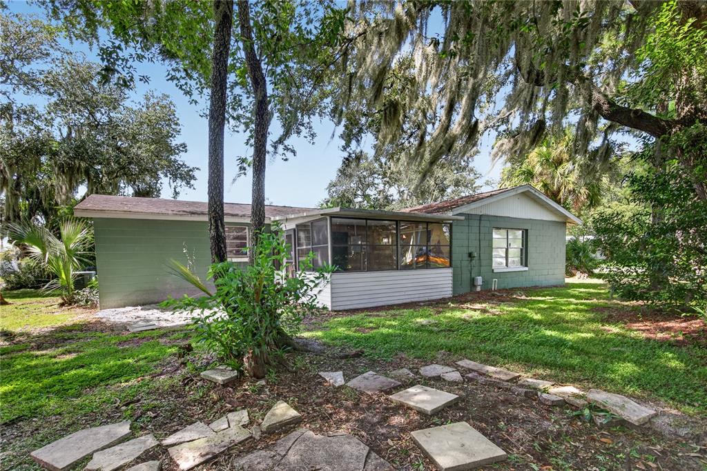 A green-painted exterior wall of a house sits near a palm tree and pine trees — 2071 CANAL ROAD, DELTONA, FL