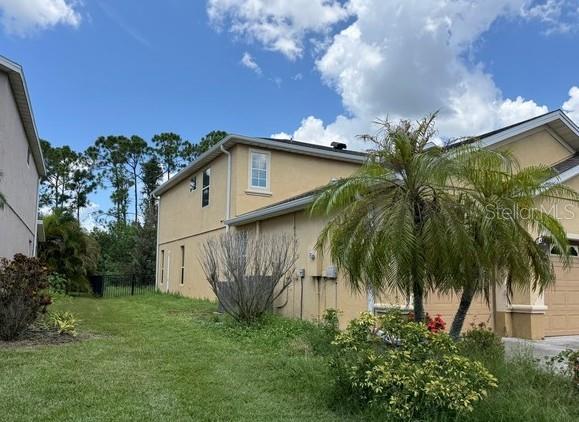 The side view of a two-story tan stucco house features a palm tree and lawn — 2531 HOBBLEBRUSH DRIVE, NORTH PORT, FL