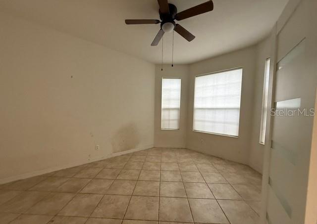 An empty room with beige tile flooring, white walls, a ceiling fan, and three windows — 2531 HOBBLEBRUSH DRIVE, NORTH PORT, FL