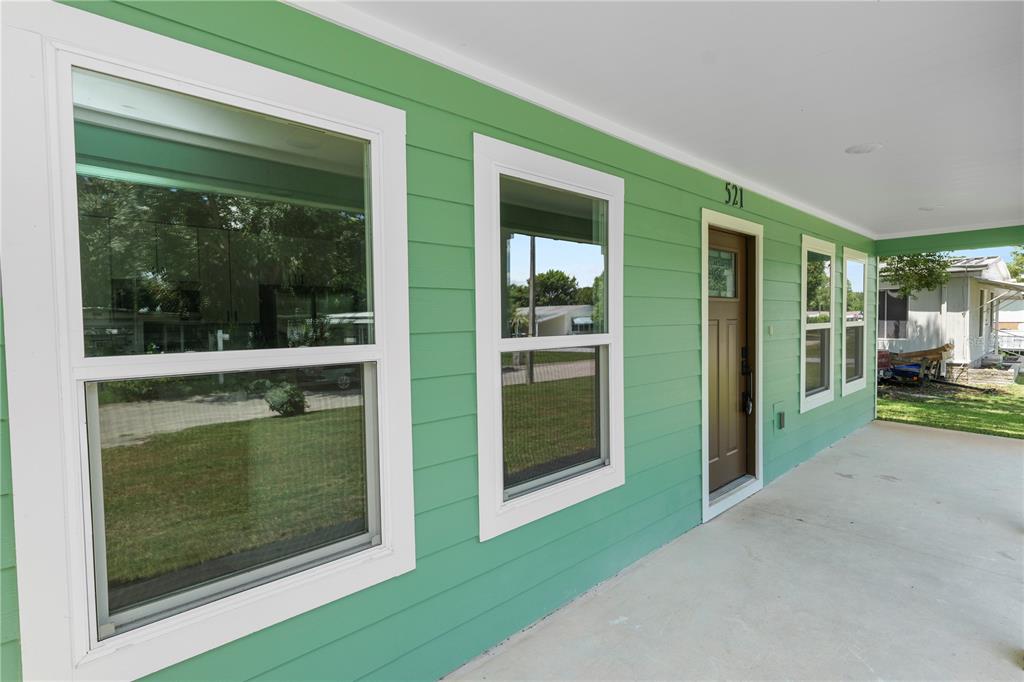 A green-sided house features a covered concrete porch, white-trimmed windows, and a brown front door — 521 SKYLINE DRIVE E, LAKELAND, FL