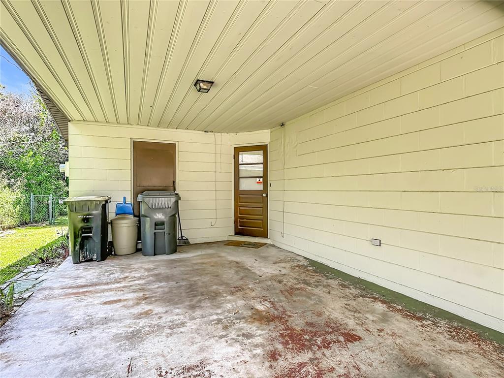 A covered concrete patio features two trash bins, a brown door, and light-colored siding — 220 PINEHURST DR, AUBURNDALE, FL