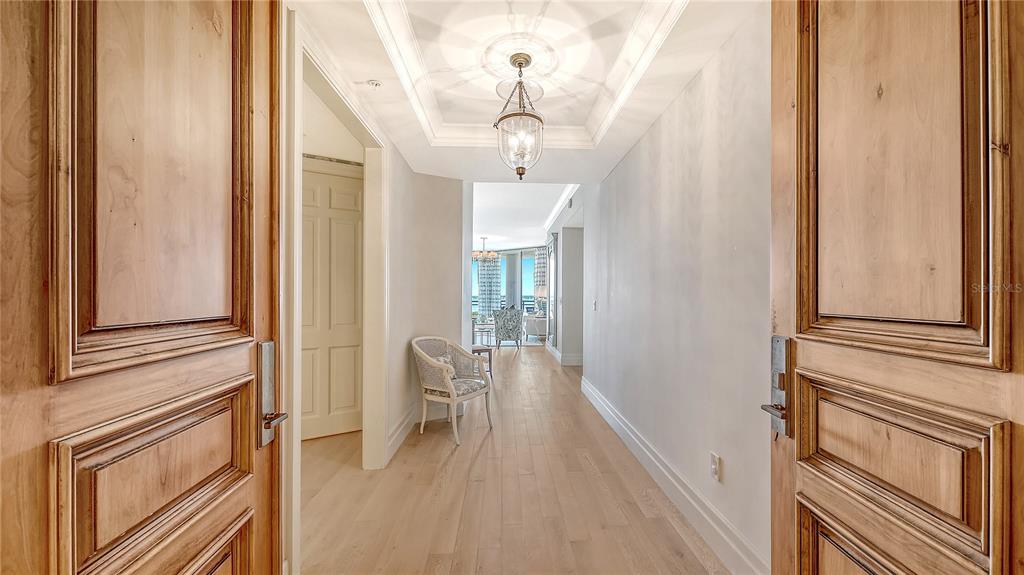 A hallway with light wood floors leads toward a bright living area with a view — 1300 BENJAMIN FRANKLIN DRIVE UNIT 908, SARASOTA, FL
