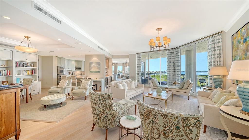A spacious, open-concept living room features light wood floors, neutral furniture, and floor-to-ceiling windows — 1300 BENJAMIN FRANKLIN DRIVE UNIT 908, SARASOTA, FL