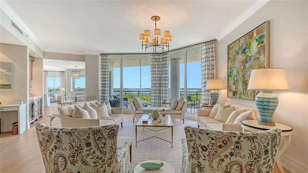 A bright living room features two sofas, patterned armchairs, a chandelier, and floor-to-ceiling windows — 1300 BENJAMIN FRANKLIN DRIVE UNIT 908, SARASOTA, FL