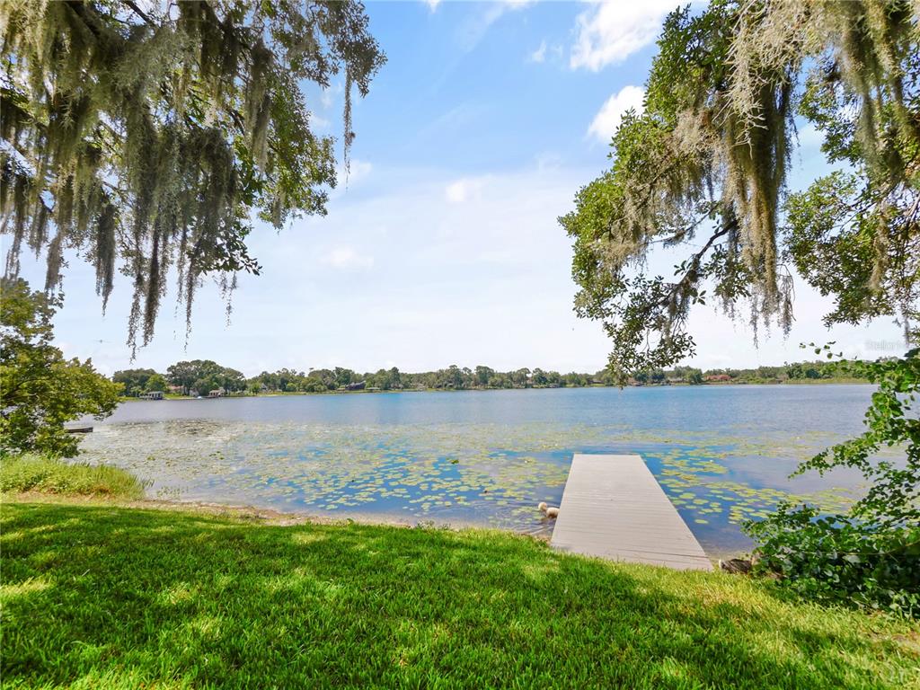 A single-story white house with blue shutters sits behind a stone walkway and large trees — 5701 CROSS FOX LANE, OVIEDO, FL