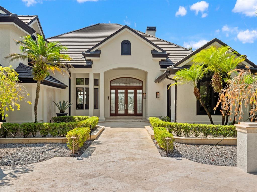 The exterior of a single-story house features a stone walkway, manicured hedges, and palm trees — 9222 SLOANE STREET, ORLANDO, FL