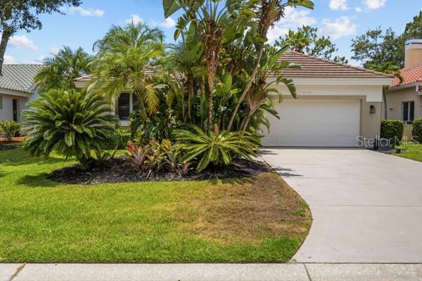A single-story house with a white garage, a concrete driveway, and lush tropical landscaping — 8710 54TH AVENUE E, BRADENTON, FL