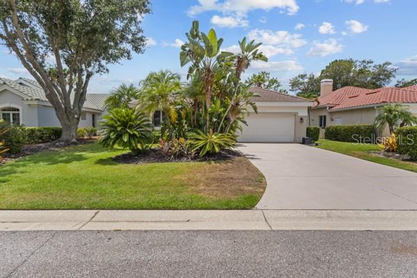 A single-story house with a concrete driveway, a two-car garage, and lush tropical landscaping — 8710 54TH AVENUE E, BRADENTON, FL
