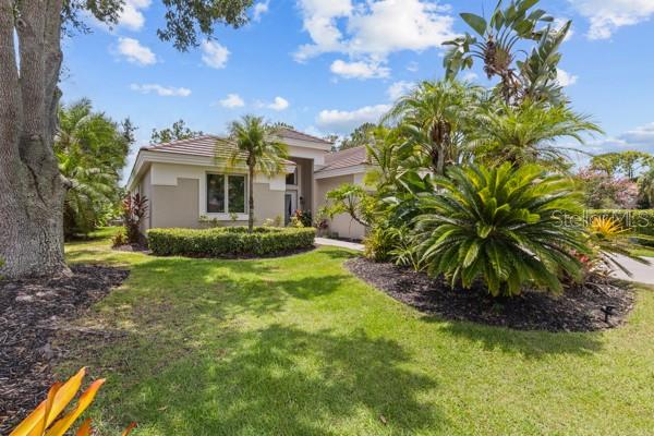 A single-story house with a tan exterior, a tiled roof, and lush tropical landscaping — 8710 54TH AVENUE E, BRADENTON, FL