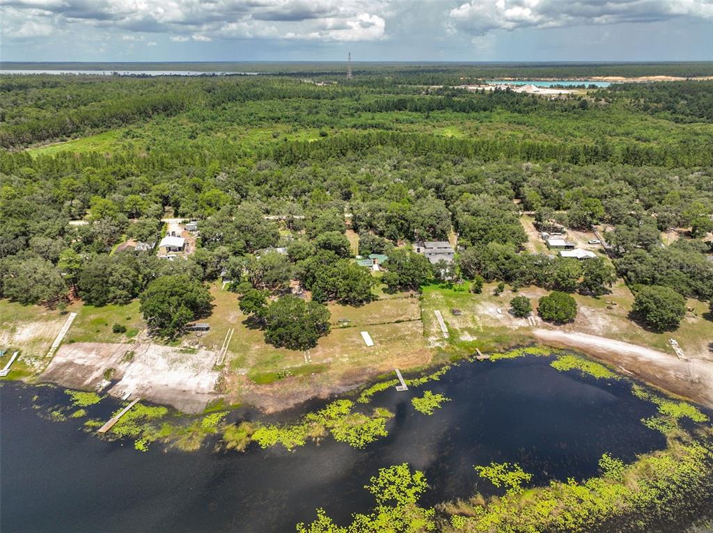 An aerial view shows a lakefront property with several houses surrounded by dense green trees — 5919 WHITE SANDS ROAD, KEYSTONE HEIGHTS, FL