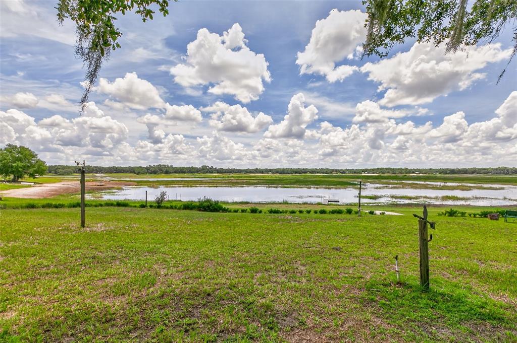 A grassy backyard overlooks a large lake under a bright blue sky with many clouds — 5919 WHITE SANDS ROAD, KEYSTONE HEIGHTS, FL