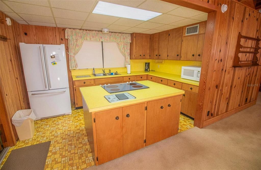 A kitchen features wood-paneled walls, yellow countertops, a central island with a cooktop, and patterned flooring — 5919 WHITE SANDS ROAD, KEYSTONE HEIGHTS, FL