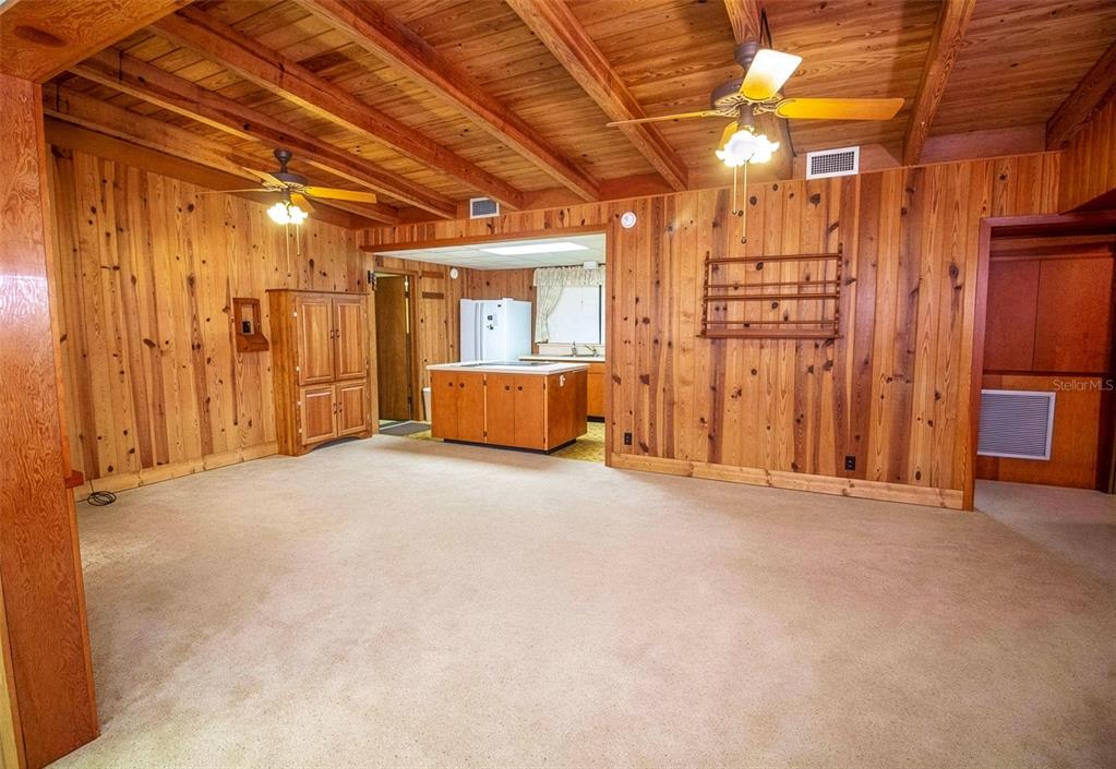 A living room with wood-paneled walls, a beamed ceiling, and an open kitchen area — 5919 WHITE SANDS ROAD, KEYSTONE HEIGHTS, FL